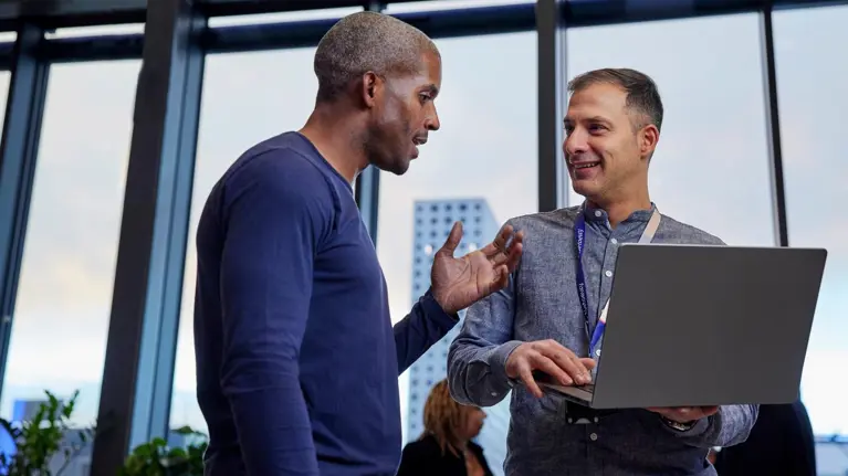 Two men discussing and smiling holding laptop