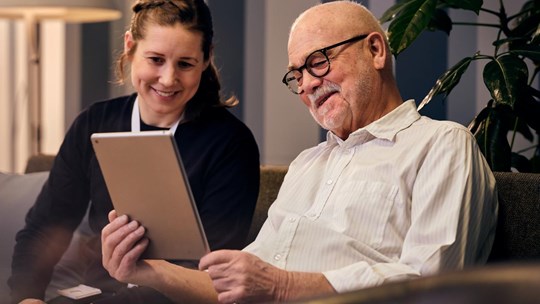 Social worker and an elderly man looking at tablet
