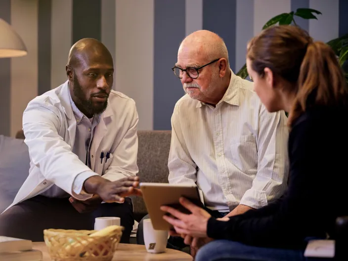 A doctor showing an elderly man information on tablet held by a social worker