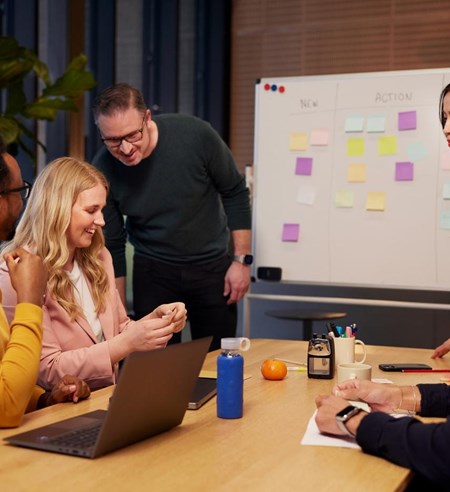 Men and women in a collaboration meeting working together using sticky notes and white board