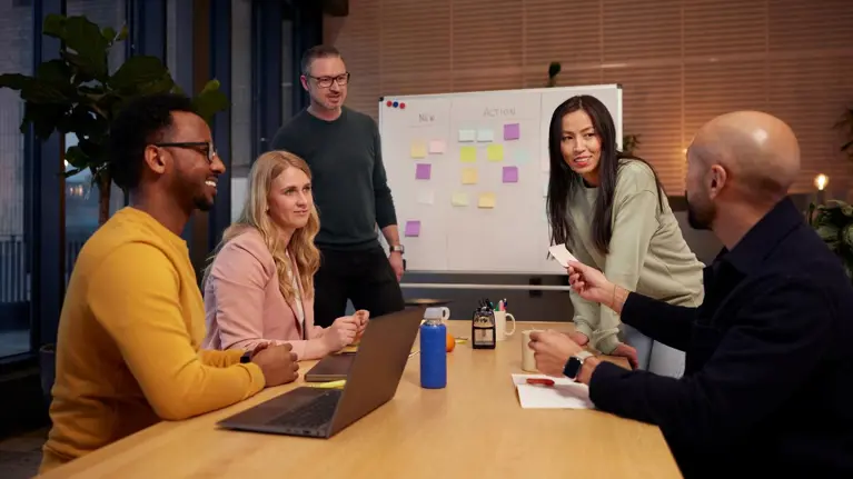 Men and women in a collaboration meeting working together using sticky notes and white board