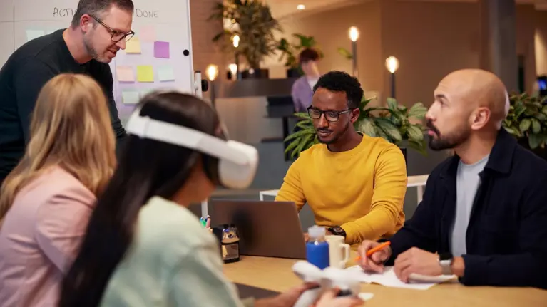 Men and women in a collaboration meeting working together using sticky notes, white board and VR head set