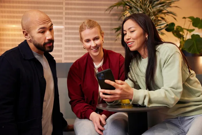 A woman is showing something on her phone to her two colleagues