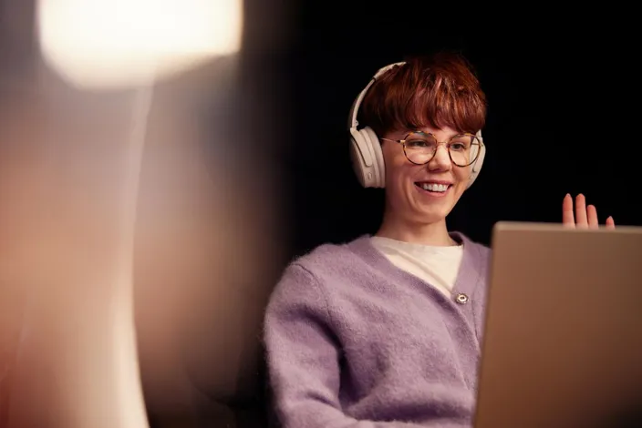 A young woman in glasses working on her laptop wearing headphones during an online meeting