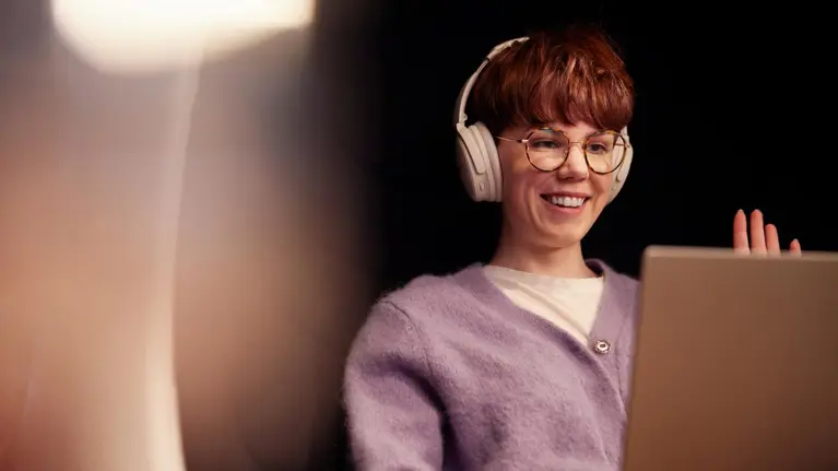 A young woman in glasses working on her laptop wearing headphones during an online meeting