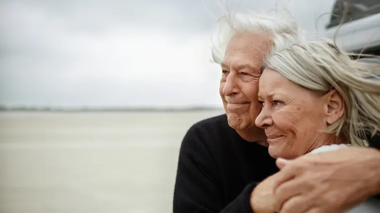 Affectionate senior couple hugging and looking away on beach