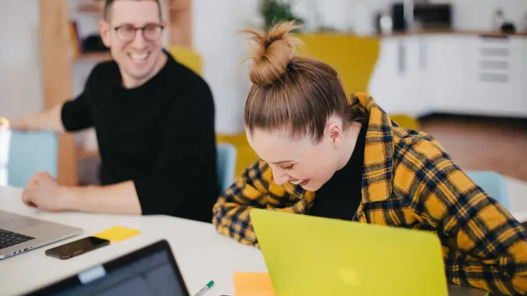 People laughing working on laptop in office