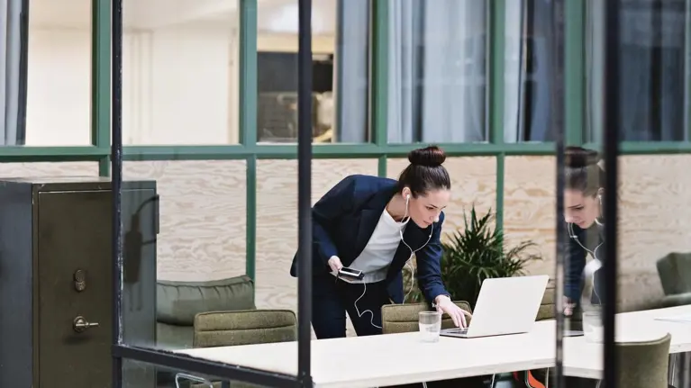 Woman talking on cellphone in headset and using laptop