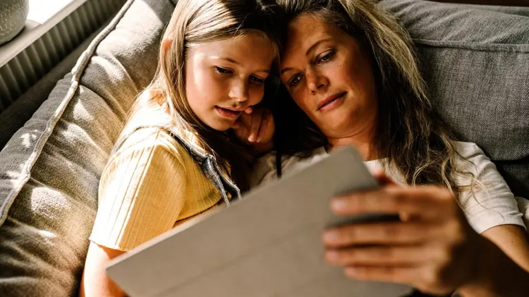 Daughter and mother on sofa at home looking at tablet browsing