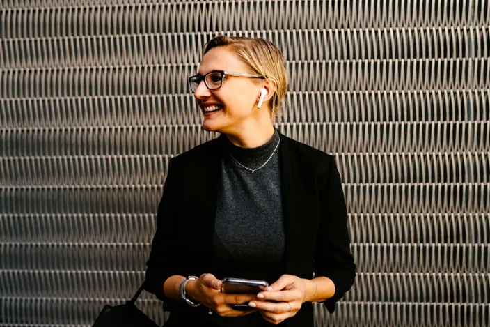 Young woman in glasses with earphones smiling using phone