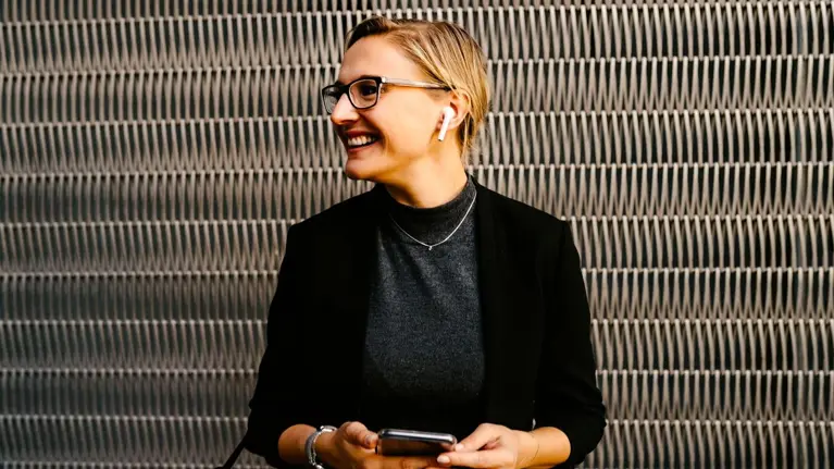 Young woman in glasses with earphones smiling using phone