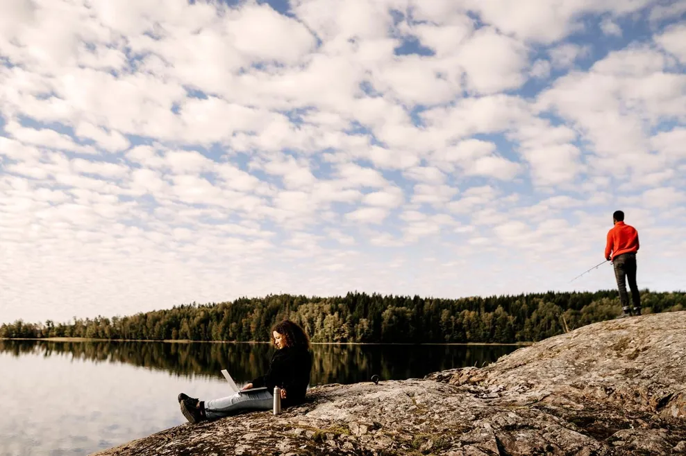 Woman working on laptop while man fishing