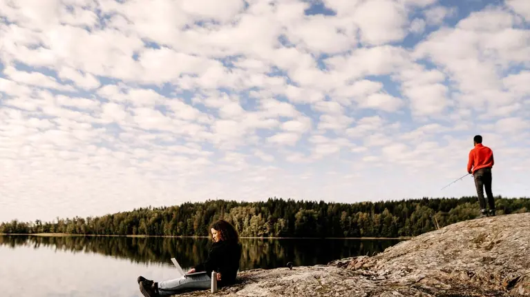 Woman working on laptop while man fishing