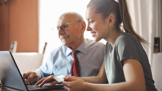 Young woman helping granddad with online banking on a laptop