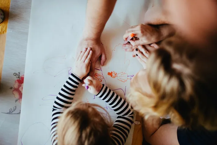 A close-up of hands of parents and kids drawing together
