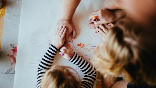 A close-up of hands of parents and kids drawing together
