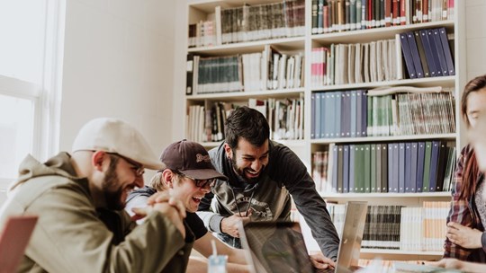 People in meeting smiling working on laptops