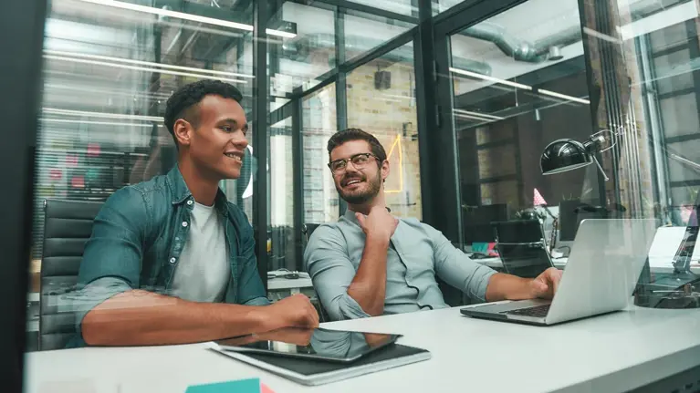 Two young men in meeting in office using laptop and tablet smiling