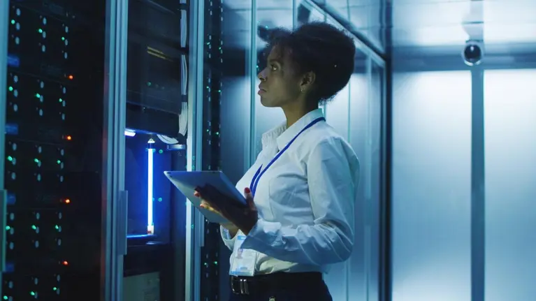 Formal African American woman using tablet while working with server rack in contemporary data center hallway