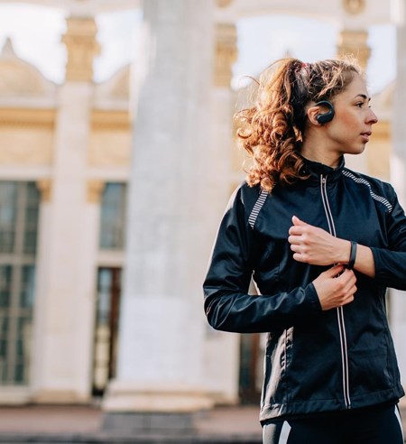 Portrait of young female athlete wearing sport jacket listening portable music player outdoors during the training session in the morning