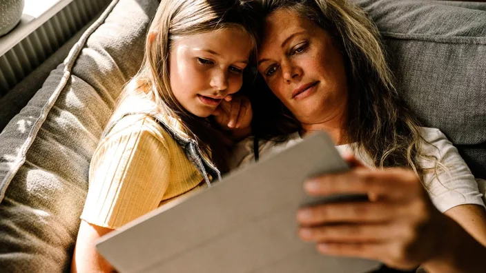 Mother and daughter lying on sofa and using tablet at home