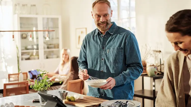 man and woman cooking in the kitchen while girls are studying in livingroom