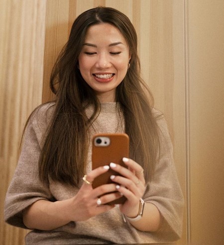 Young woman taking photo with her phone smiling siting in window