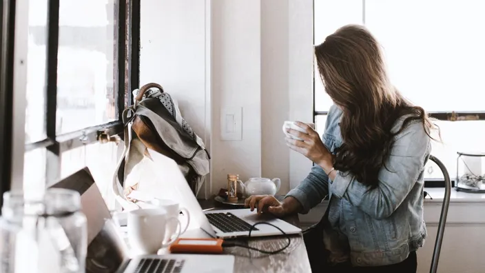 Woman drinking coffee and working on her laptop