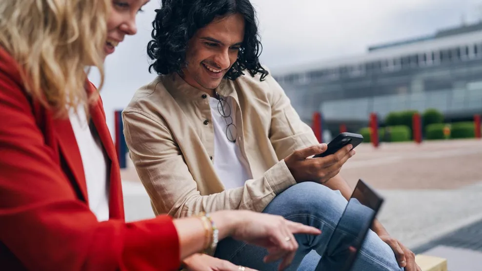 Man and woman working on laptop using cell phone smiling next to Tietoevry office building