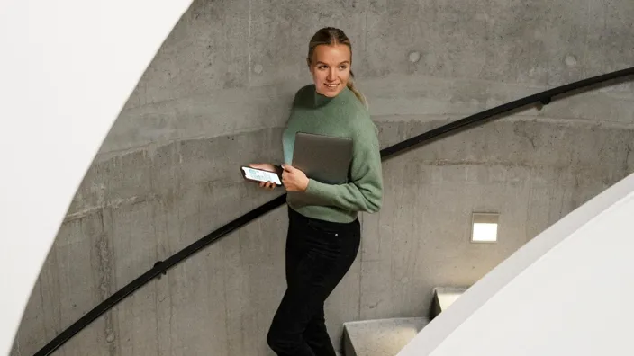 Girl walking down the stairs using phone holding laptop